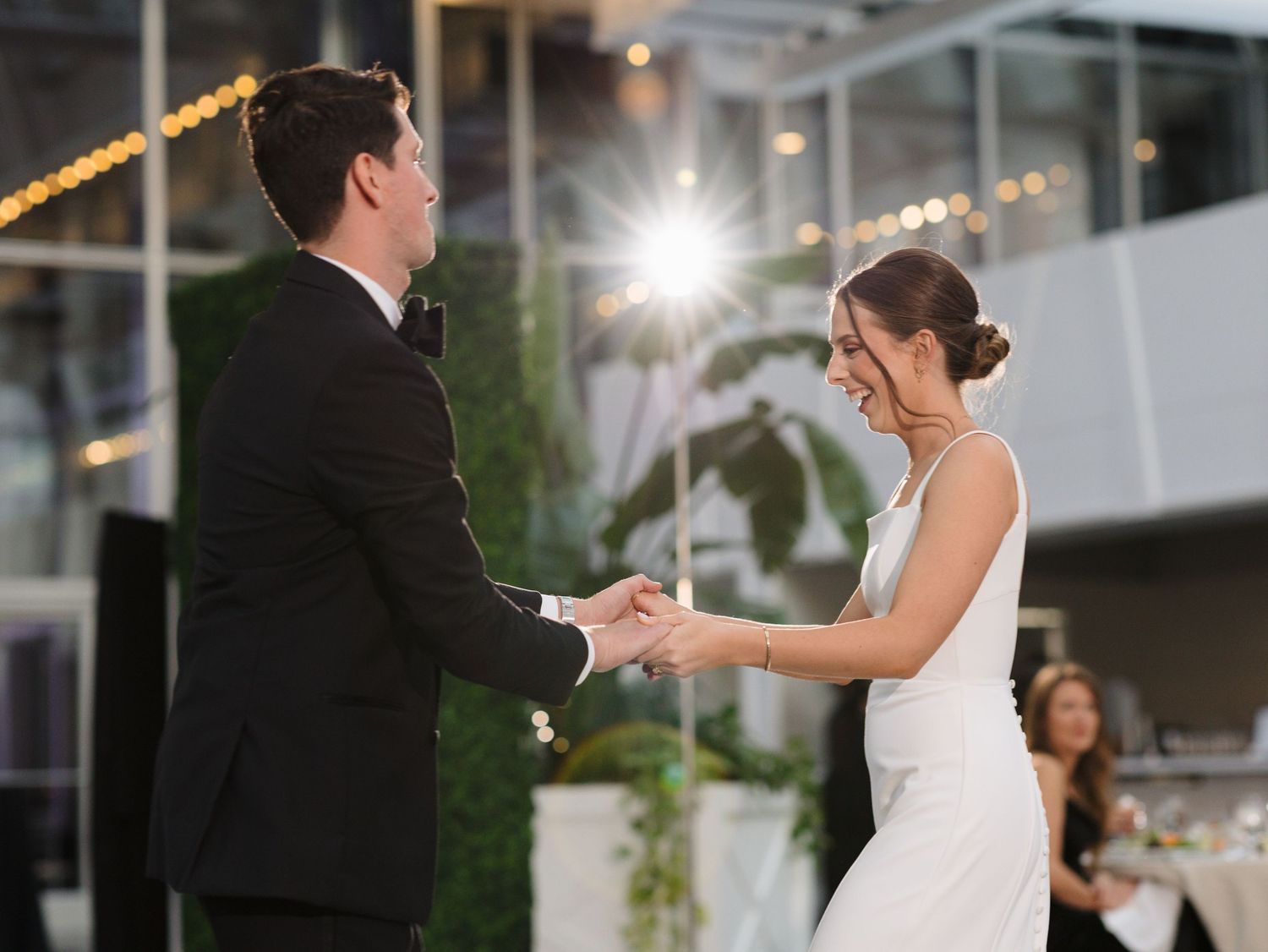 Newlyweds share a romantic dance moment on a checkered floor under twinkling lights at their reception.