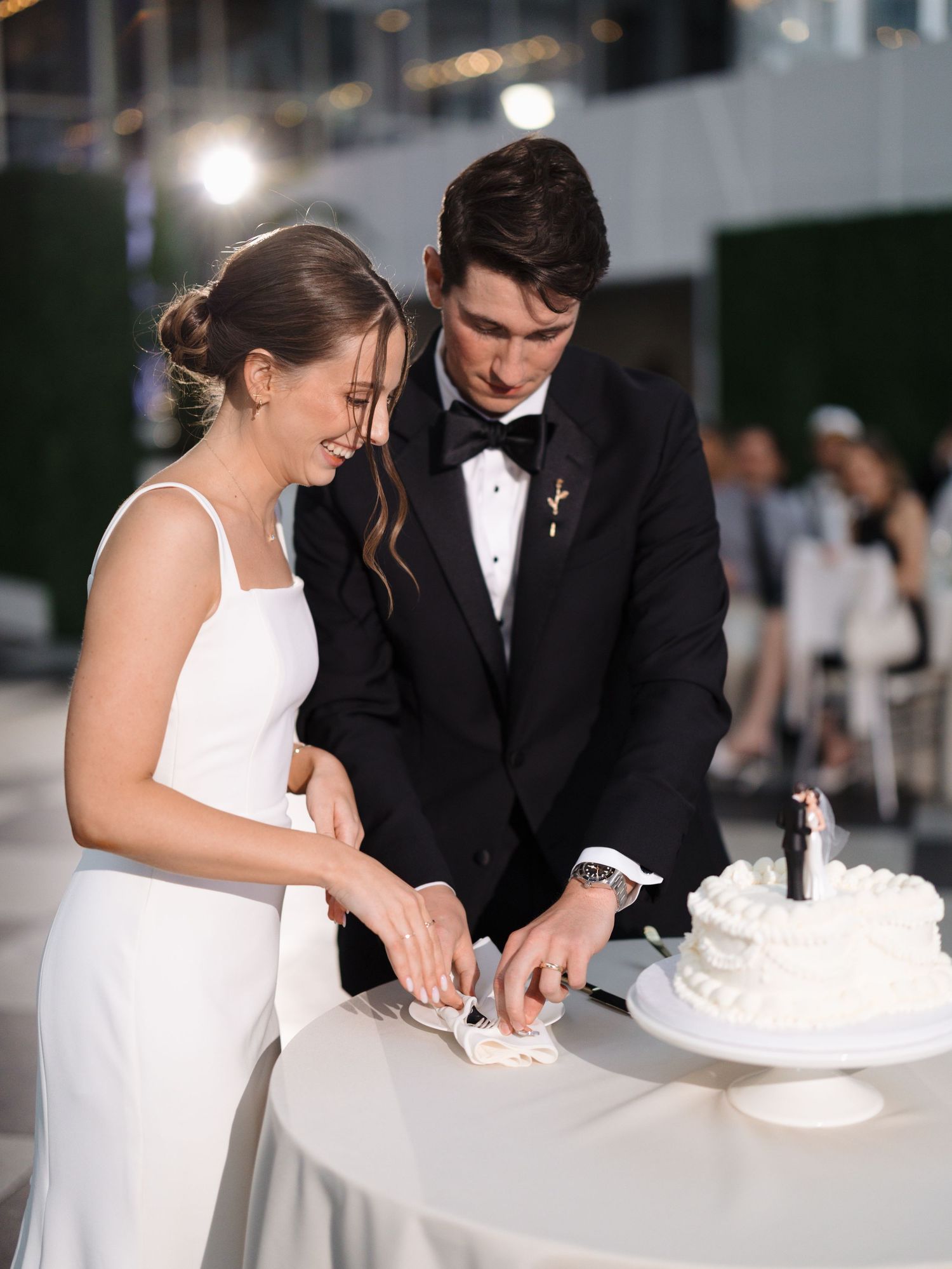 A bride and groom cut their elegant white wedding cake together during their reception celebration.
