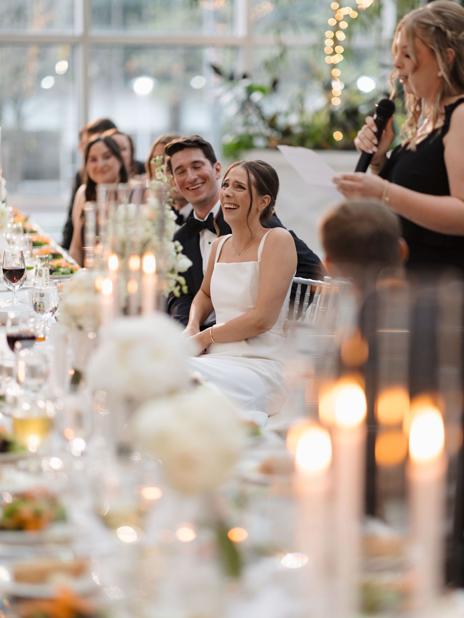 Candlelit wedding reception dinner table with guests enjoying conversation in an elegant indoor venue with twinkling lights.