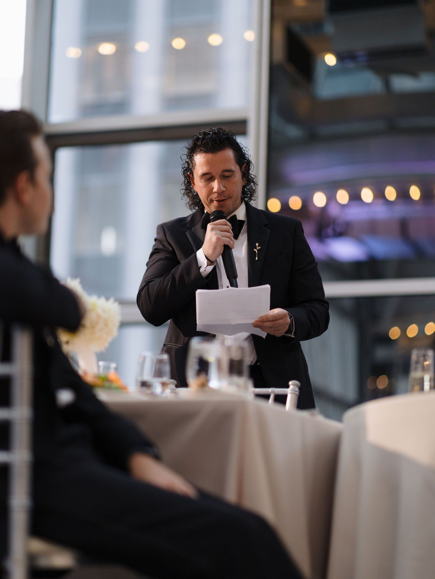 Business professional in a dark suit reviews documents while seated at an elegant restaurant table with ambient lighting.