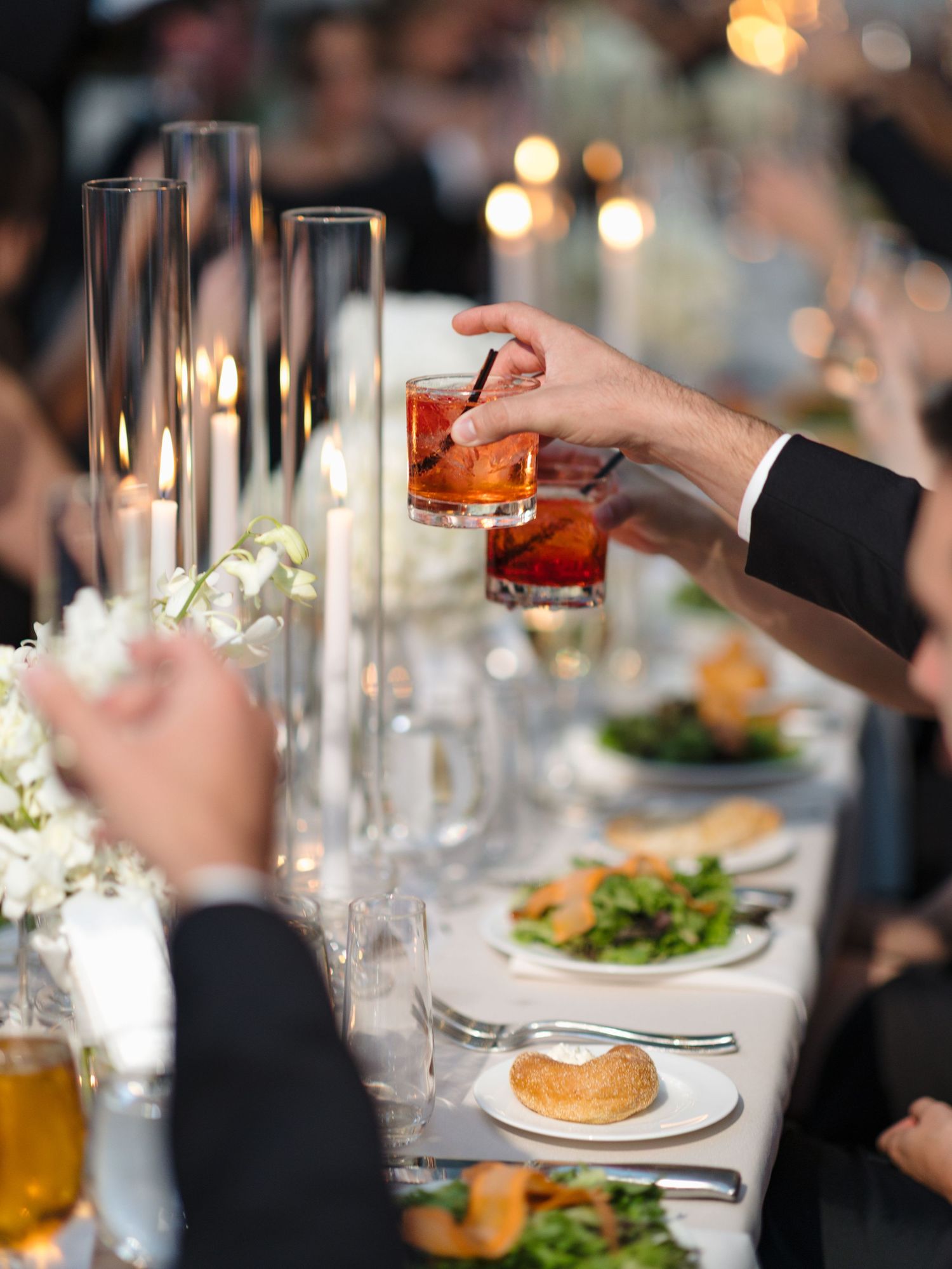 Elegant table settings at a formal dinner party with wine glasses and plated meals in warm ambient lighting.