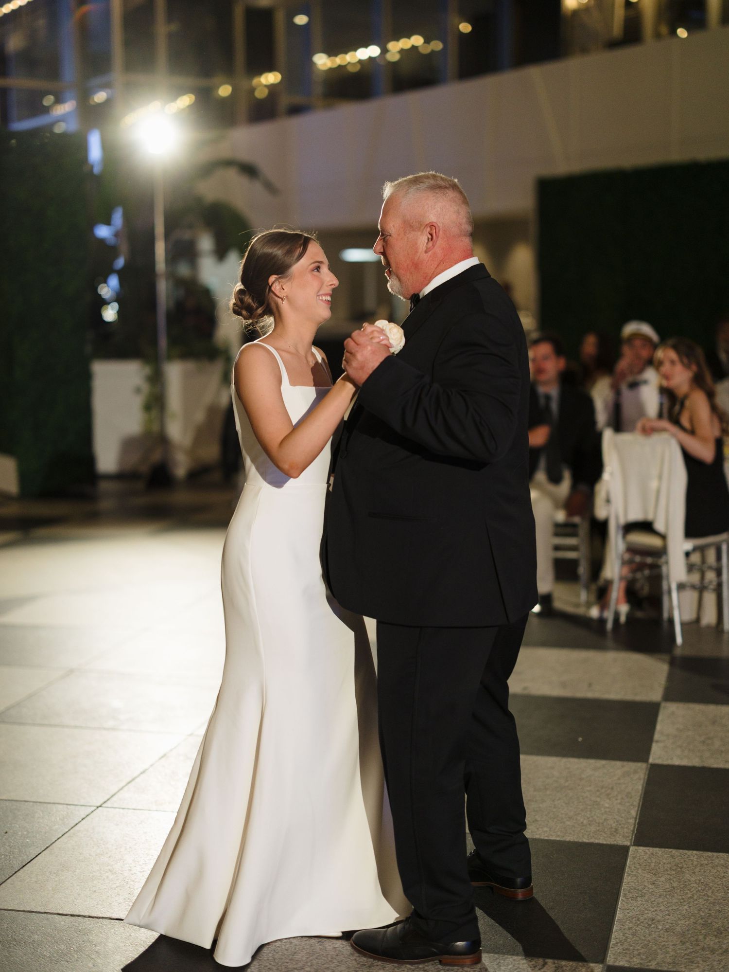 A couple shares an intimate dance moment on a black and white checkered floor at an evening reception.