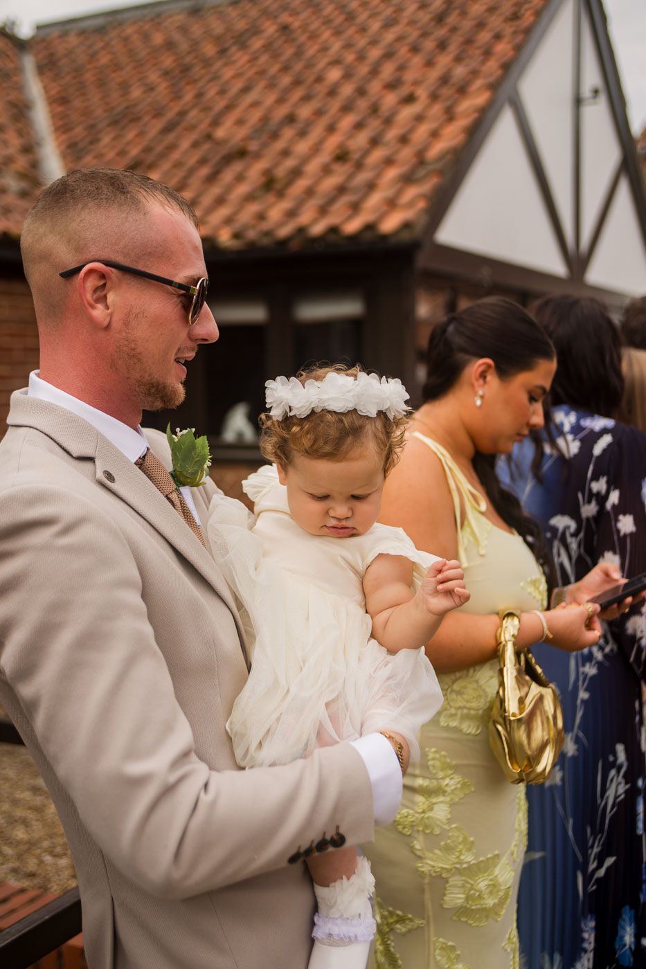A sweet moment at a wedding as a couple holds a baby in a white dress with a floral headband.