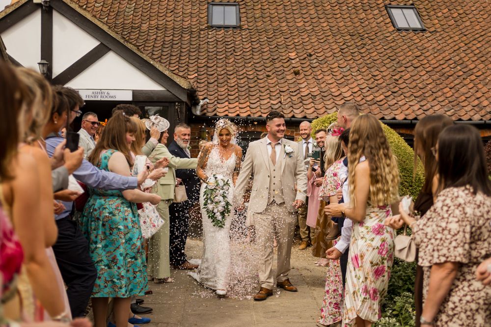 Wedding guests in colorful summer dresses gather outside a venue with terra cotta roof tiles.