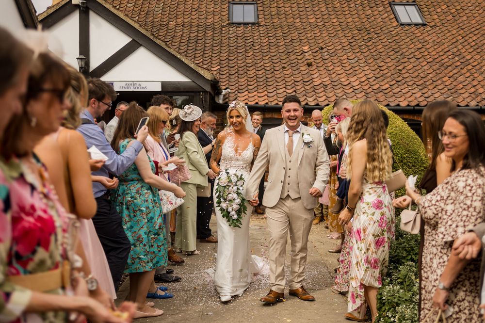 Wedding guests line up outside a rustic venue with terra cotta roofing.