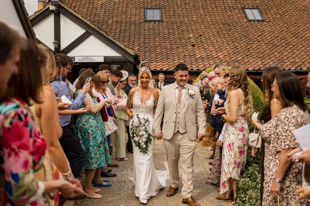 Guests in floral dresses form lines outside a wedding venue with traditional architecture.