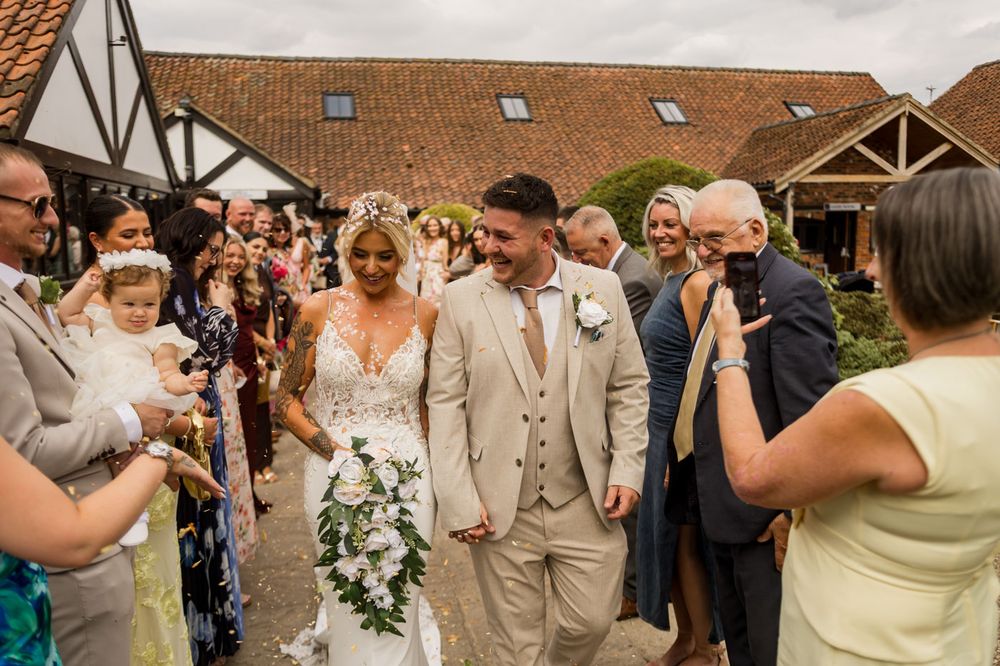 Guests take photos of the wedding party outside a rustic venue with terra cotta roof.