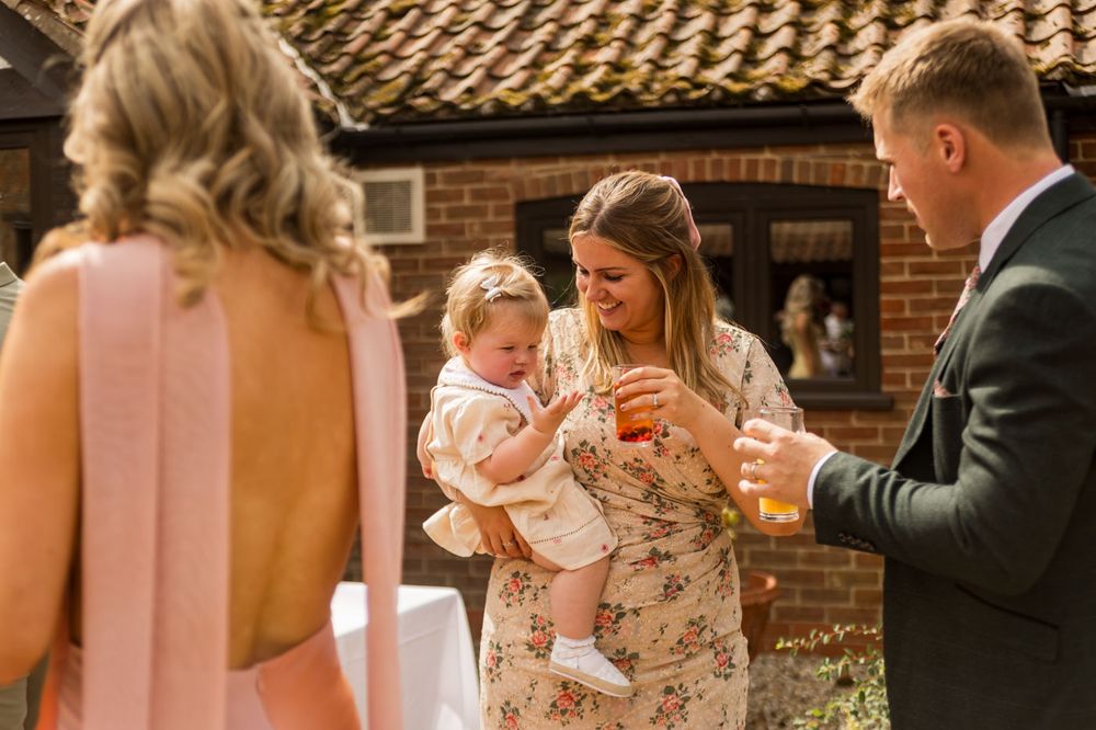 Wedding guests gather outside a rustic brick building with terra cotta roofing.