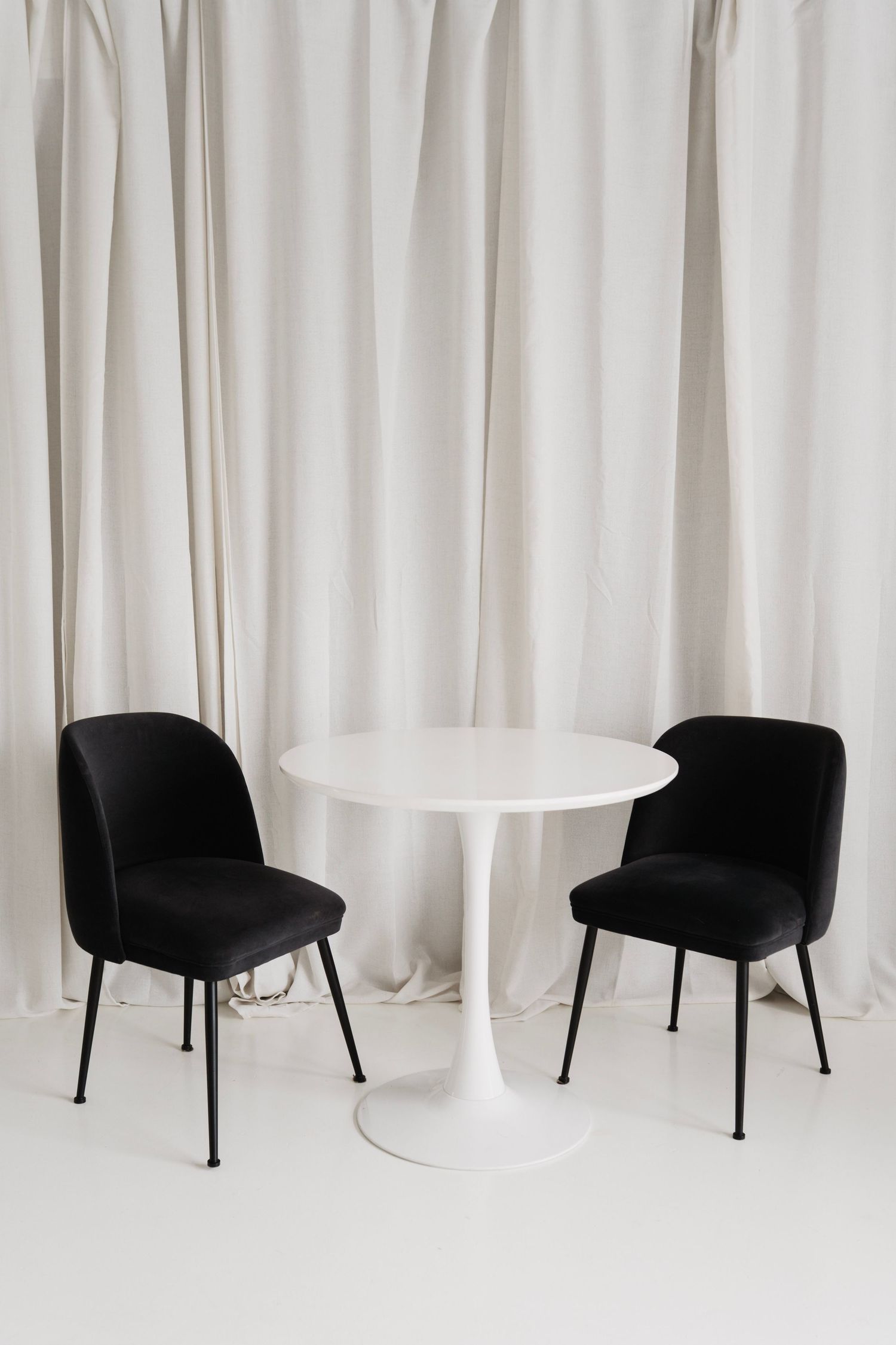 Modern black accent chair with curved backrest against white curtain backdrop in minimalist setting.