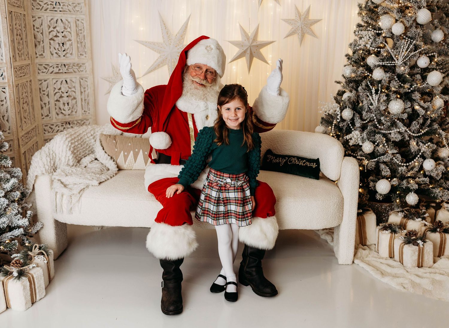 A festive holiday photo set featuring a white and gold Christmas backdrop with decorated trees and Santa's chair.