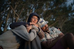 Two people rest together outdoors wrapped in blankets during golden hour.