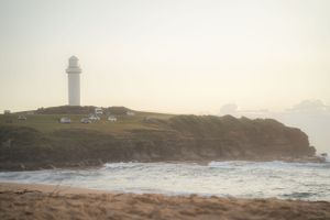 Lighthouse on rocky coastal cliffs during a misty sunset.