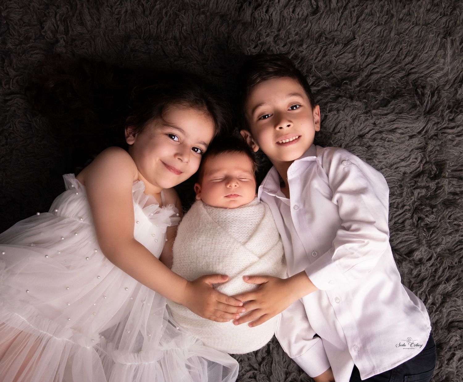 Intimate maternity photo series with couple in white clothing against dark backdrop.