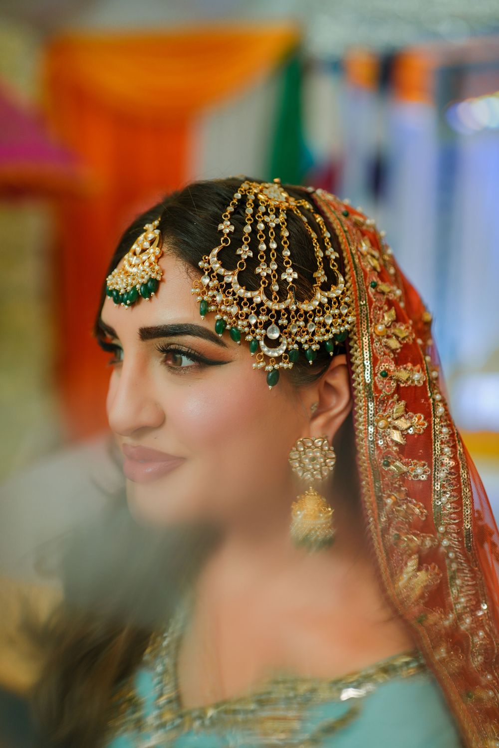 Traditional South Asian bridal jewelry and headpiece details in gold with emerald accents against a turquoise outfit.