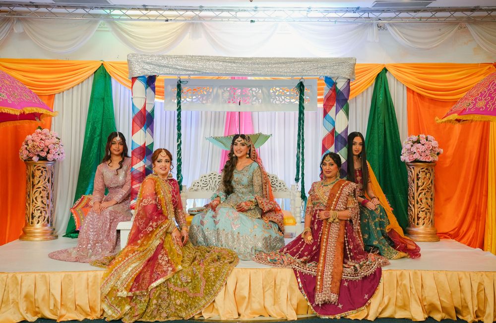 Traditional South Asian celebration with colorful orange and green drapes featuring decorative stage setup for an elegant event.
