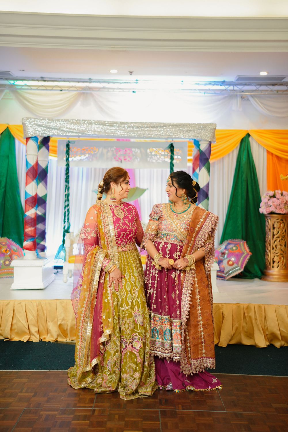 Two guests in colorful traditional outfits chat during celebration with festive decorations.