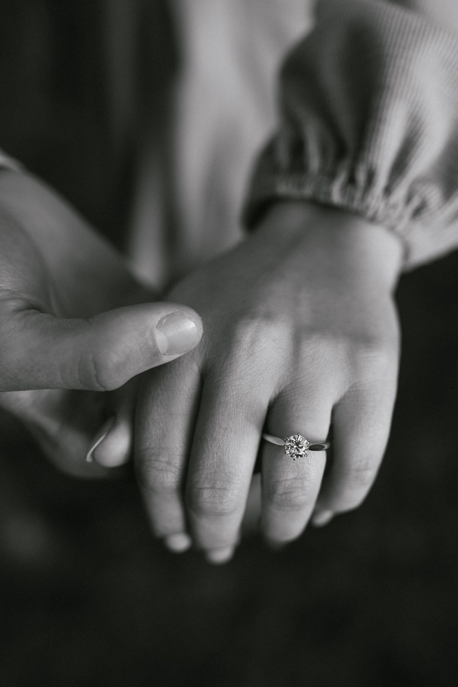 Black and white close-up of hands showing off an engagement ring.
