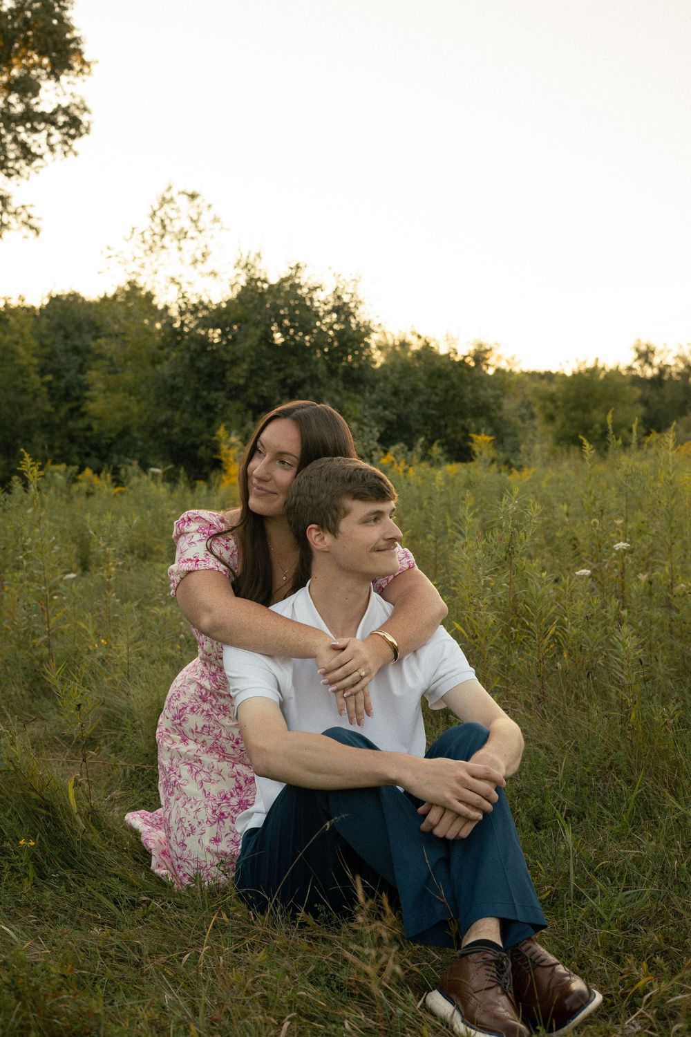 A couple sits in a green flower meadow during their engagement photos in Ann Arbor, Michigan in August.