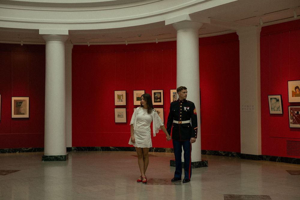 A couple holds hands as they take engagement photos inside of an art museum in Ann Arbor, Michigan.