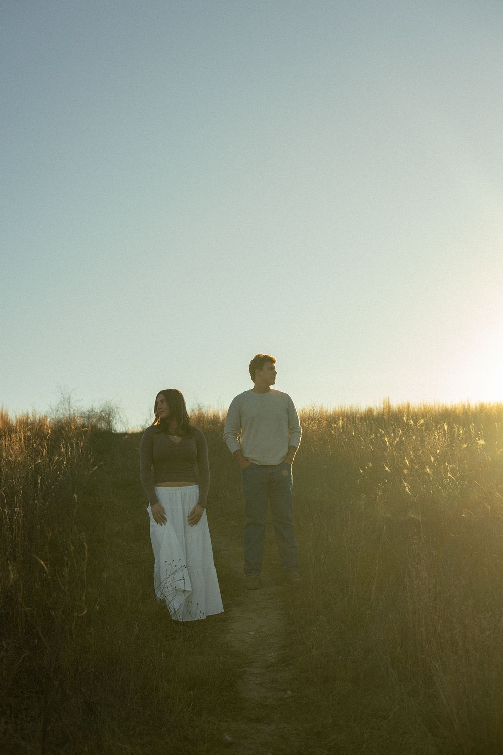Two silhouettes walk through a golden field at sunset creating a romantic countryside scene during couples photos in Brighton, MI.