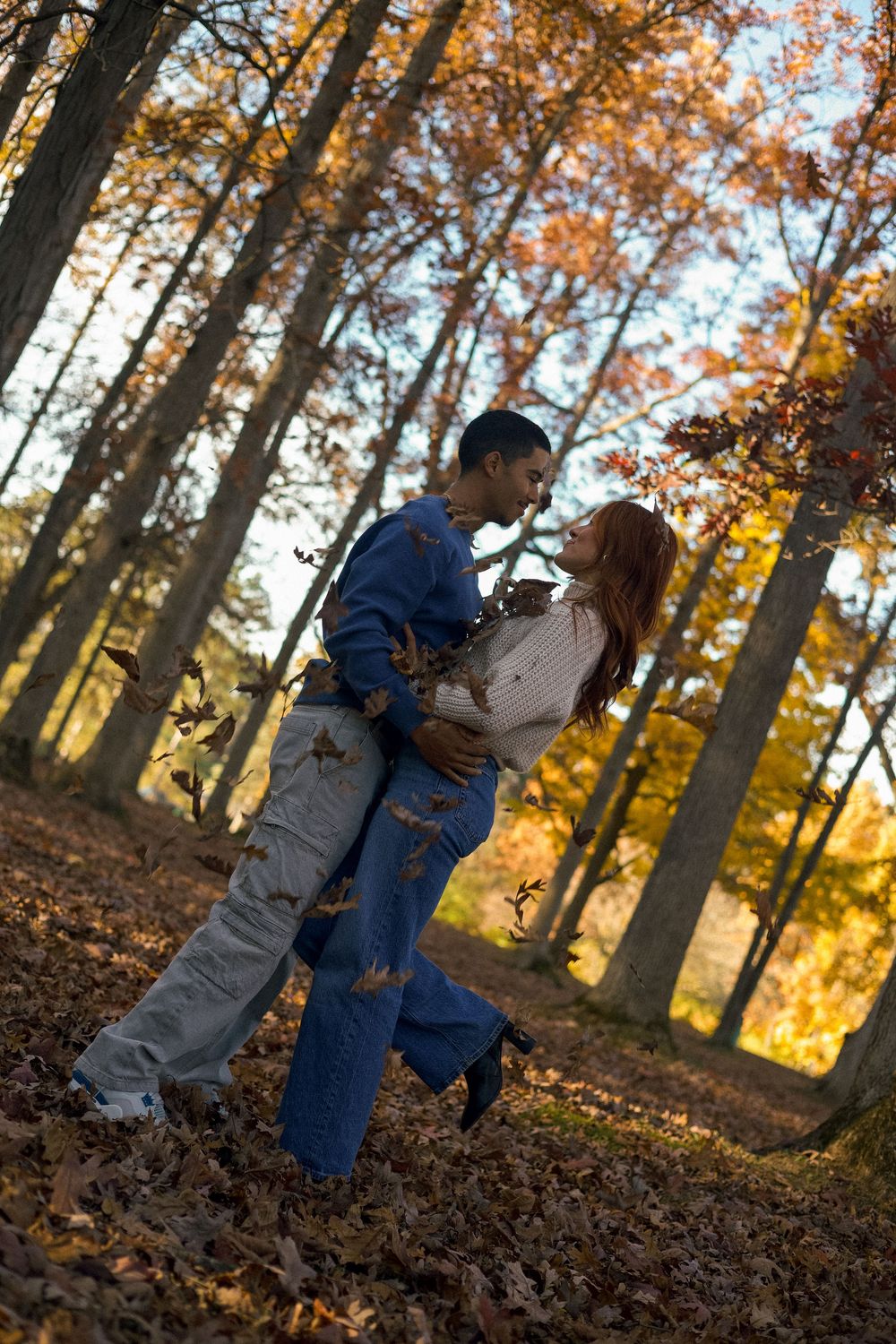 A couple laughs and embraces as leaves fall during their autumn engagement session in Flushing, Michigan.