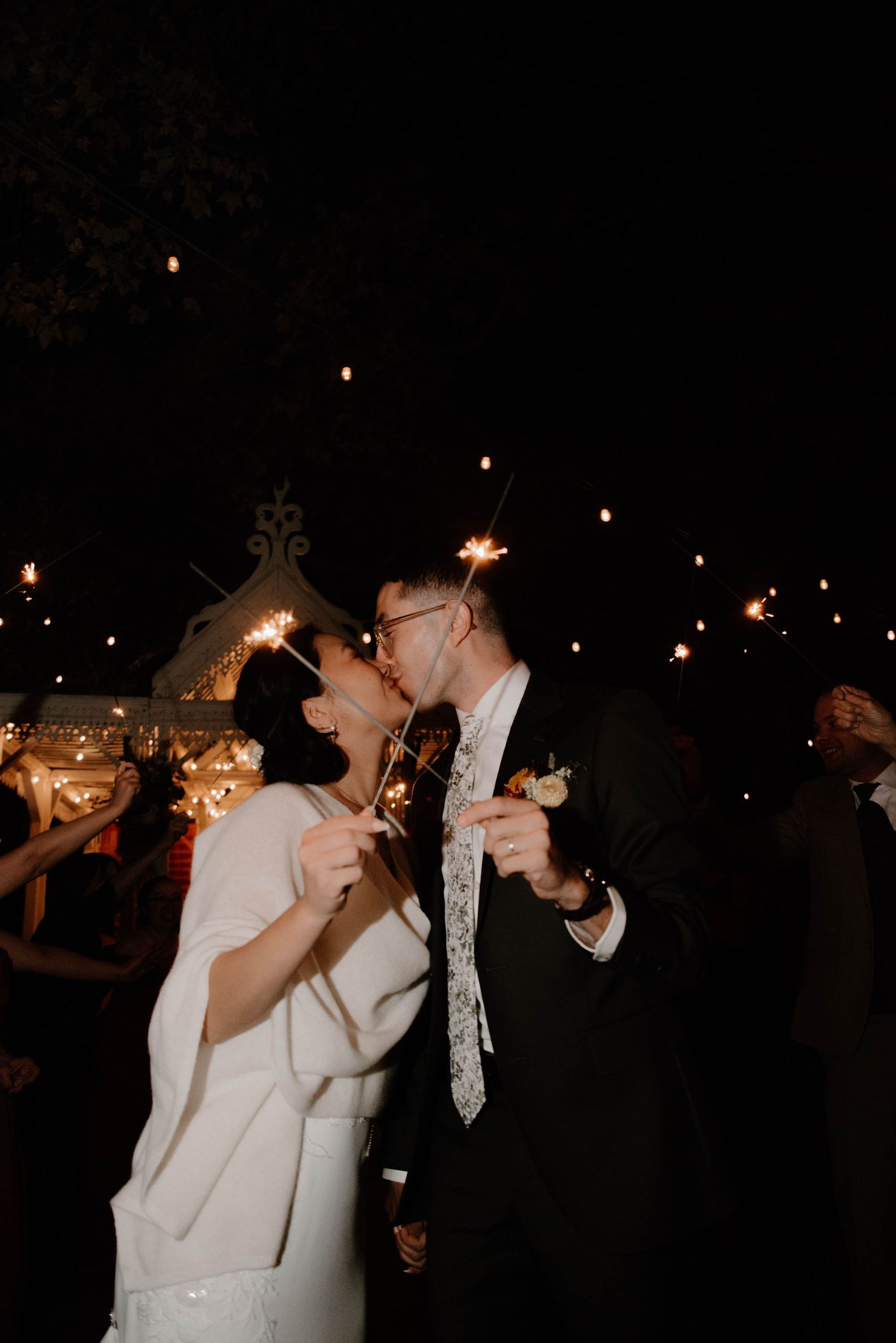 A couple shares a romantic moment under string lights at a nighttime celebration.