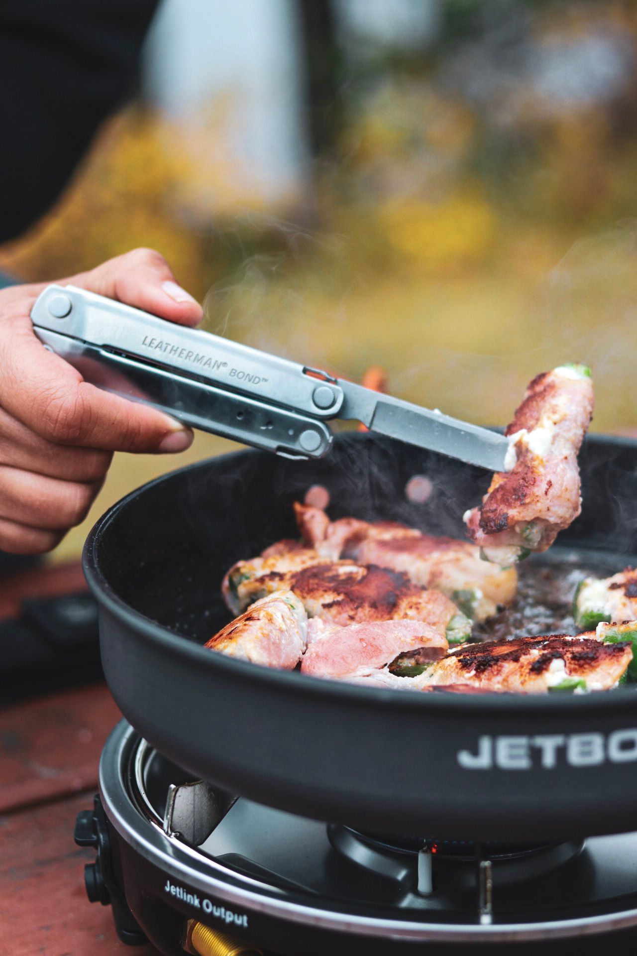 Multi-tool being used to flip meat on a Jetboil camping stove outdoors.