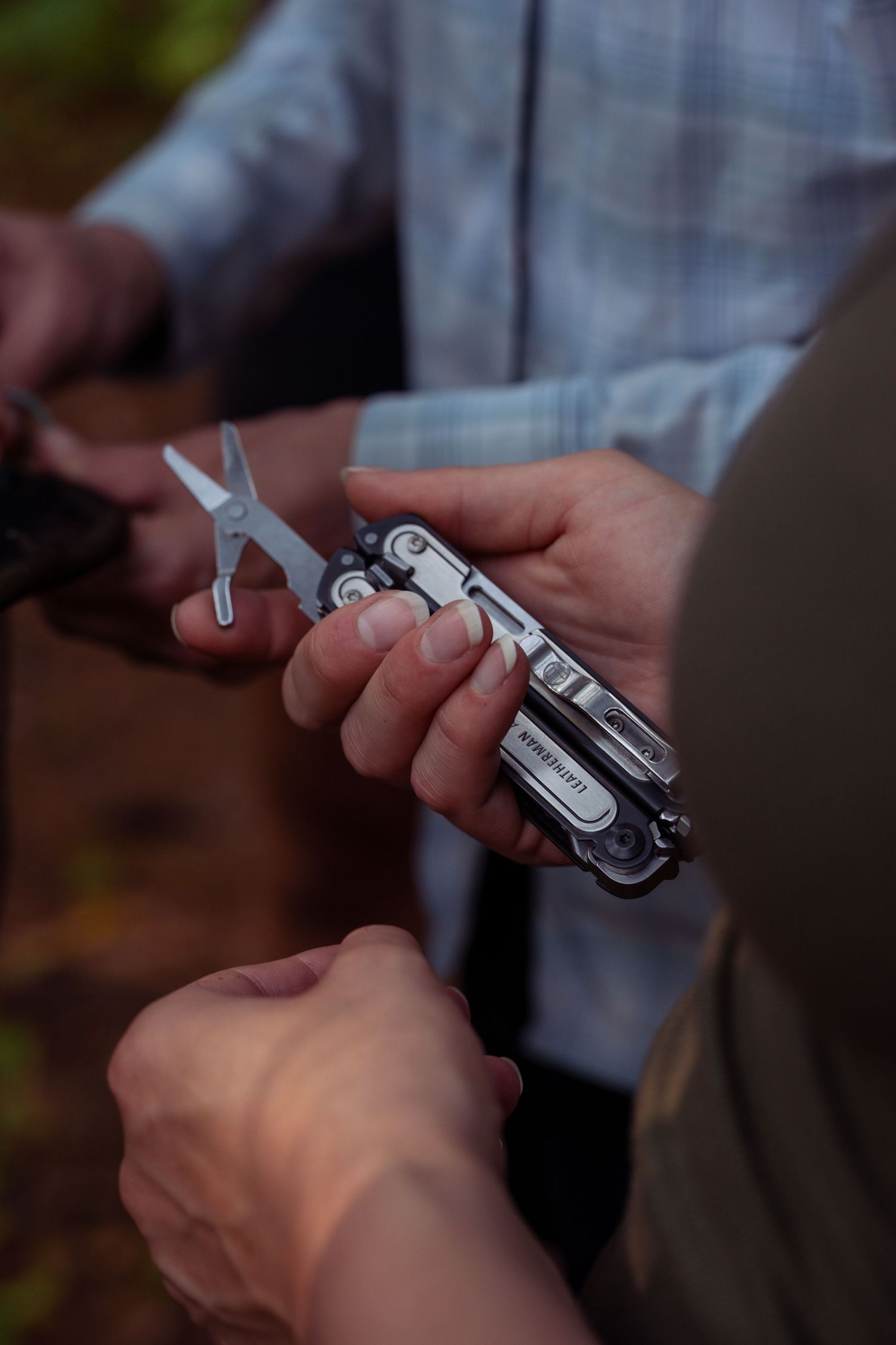 Close-up of hands holding and adjusting a metal multi-tool outdoors.