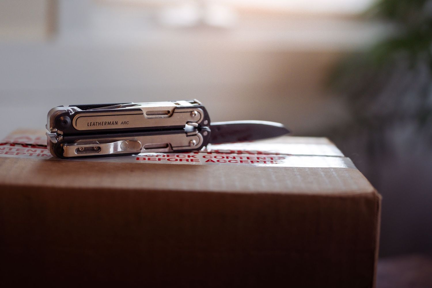 Silver pocket multi-tool resting on brown leather surface in soft focus.