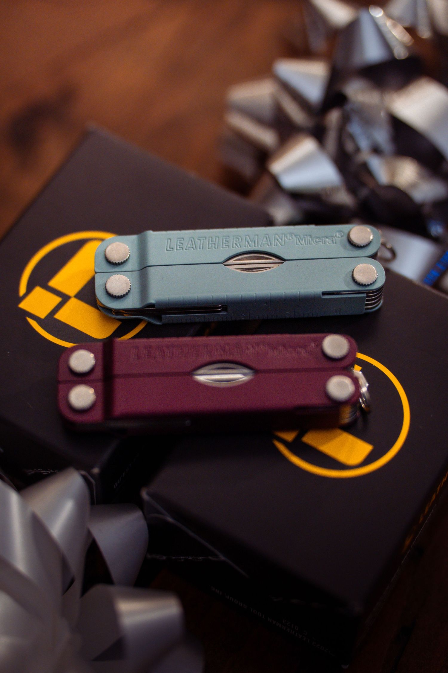 Two Leatherman multi-tools in different colors displayed on gift boxes with silver bows.