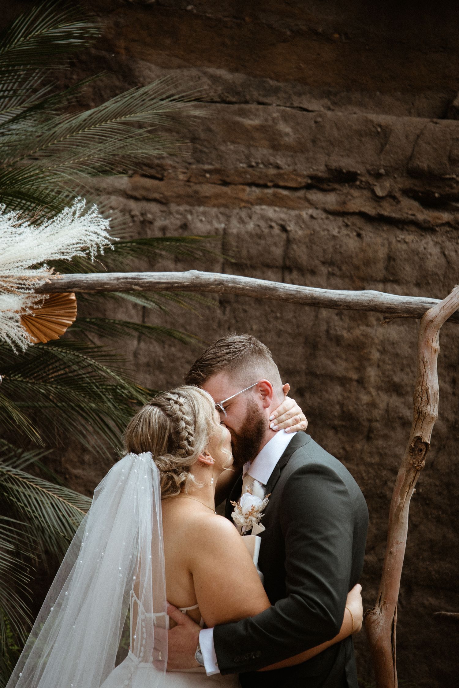 A romantic wedding moment between newlyweds against a natural rock wall backdrop.