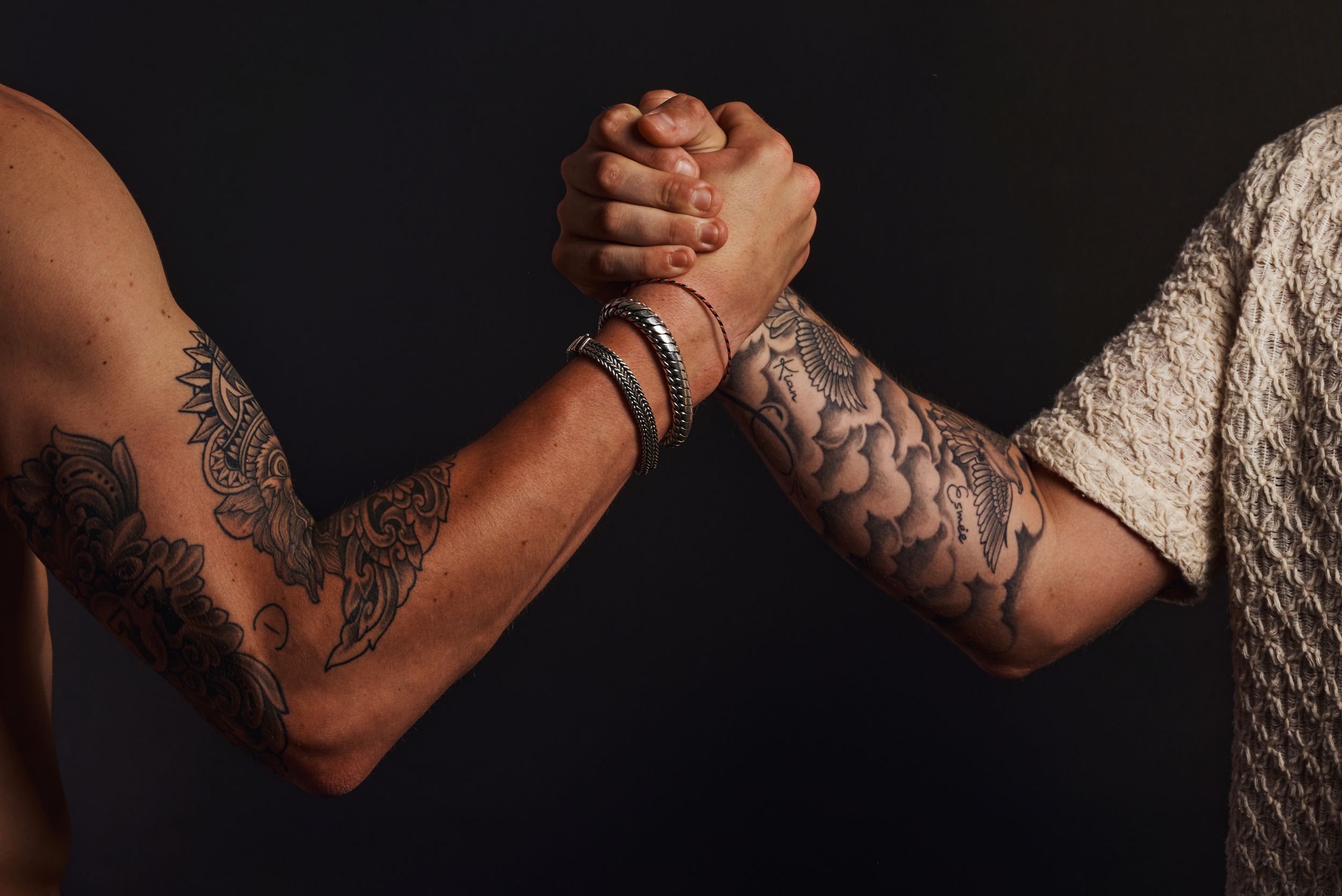 Close-up van twee getatoeëerde armen met een sterke handdruk.