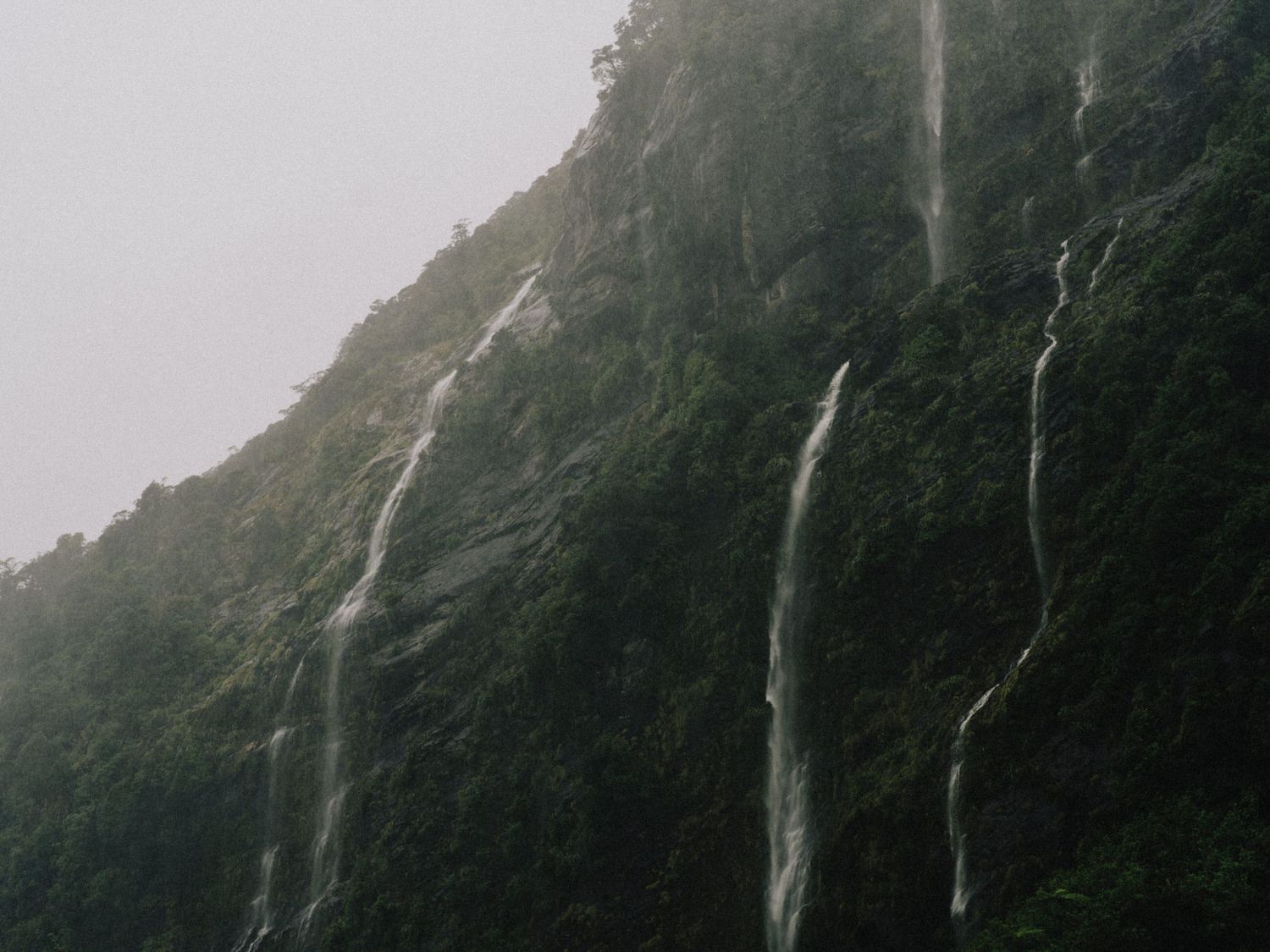 Multiple waterfalls cascade down a steep mountainside shrouded in mist.