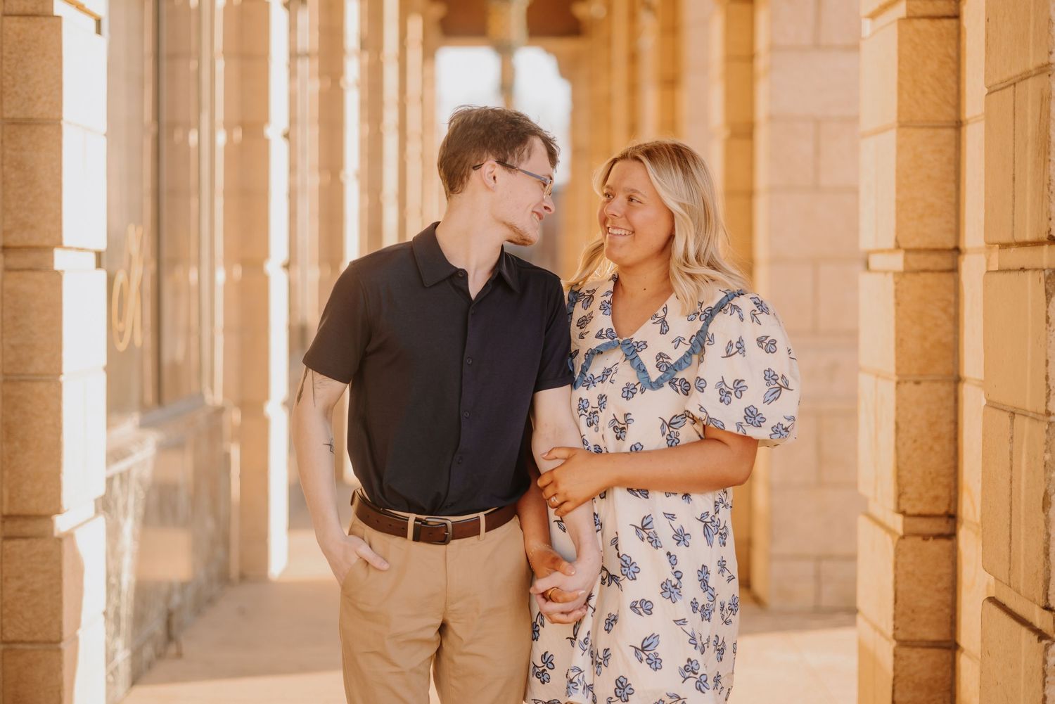 Couple embraces in warm sunlit corridor with elegant architectural columns.