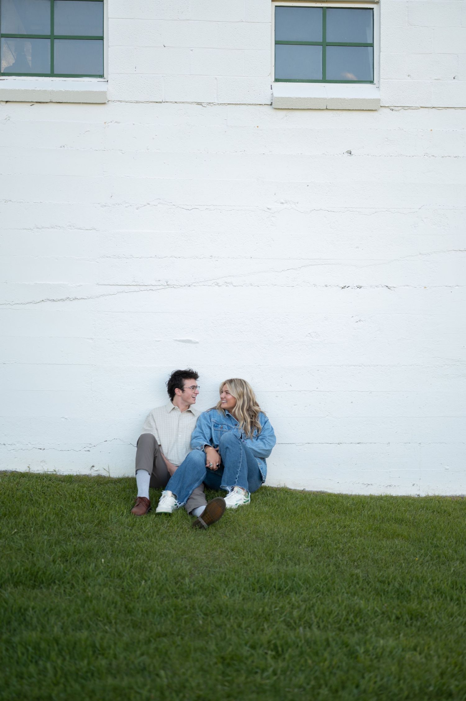 Couple sitting and relaxing against white wall with green grass in foreground.