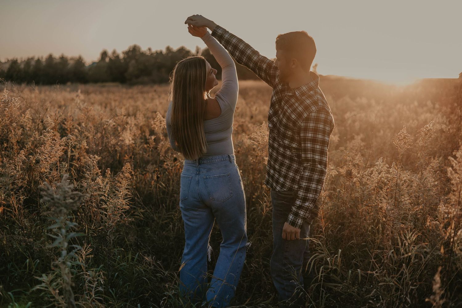 Couple dancing in golden field at sunset during romantic photoshoot.