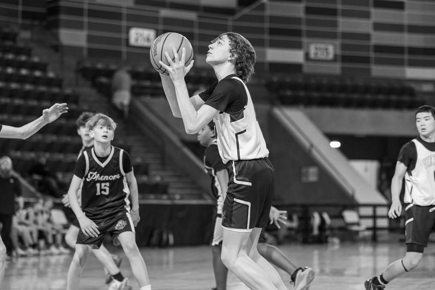Black and white photo of youth basketball players in action during an indoor game.