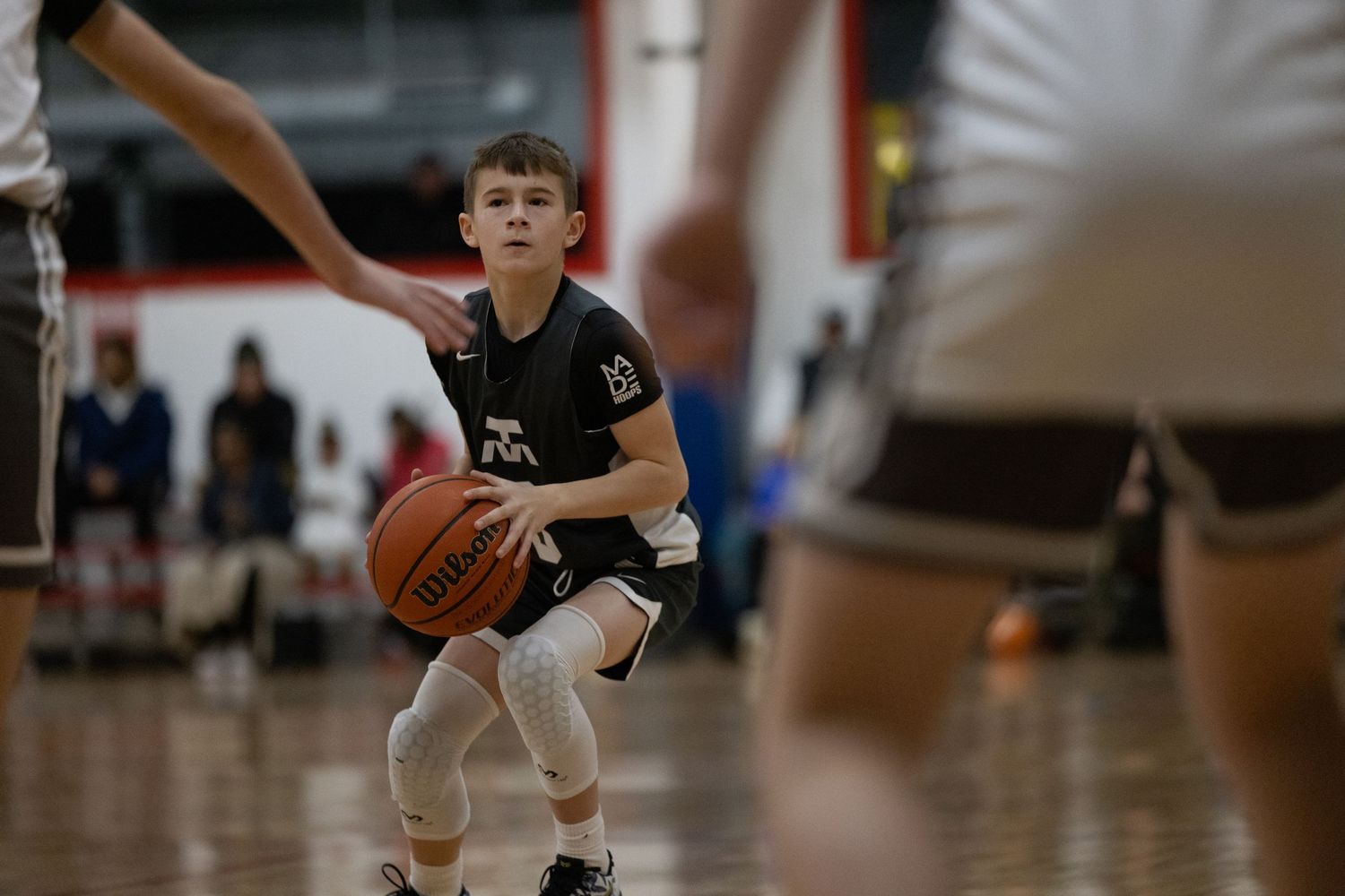 Young player protectively cradles basketball while preparing to shoot during indoor youth basketball game.