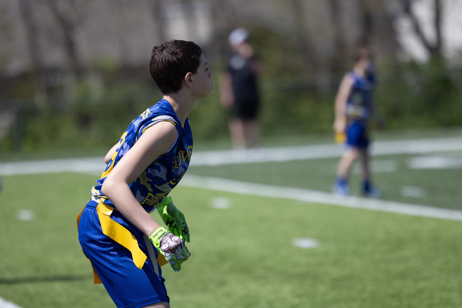 Youth athlete in blue and yellow uniform stands ready on a sports field during gameplay.