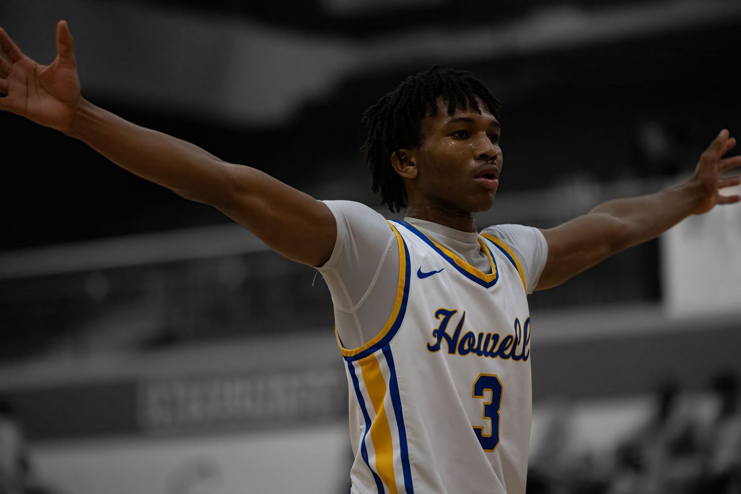 A basketball player in a white and gold jersey with number 3 raises their arms in celebration during a game.
