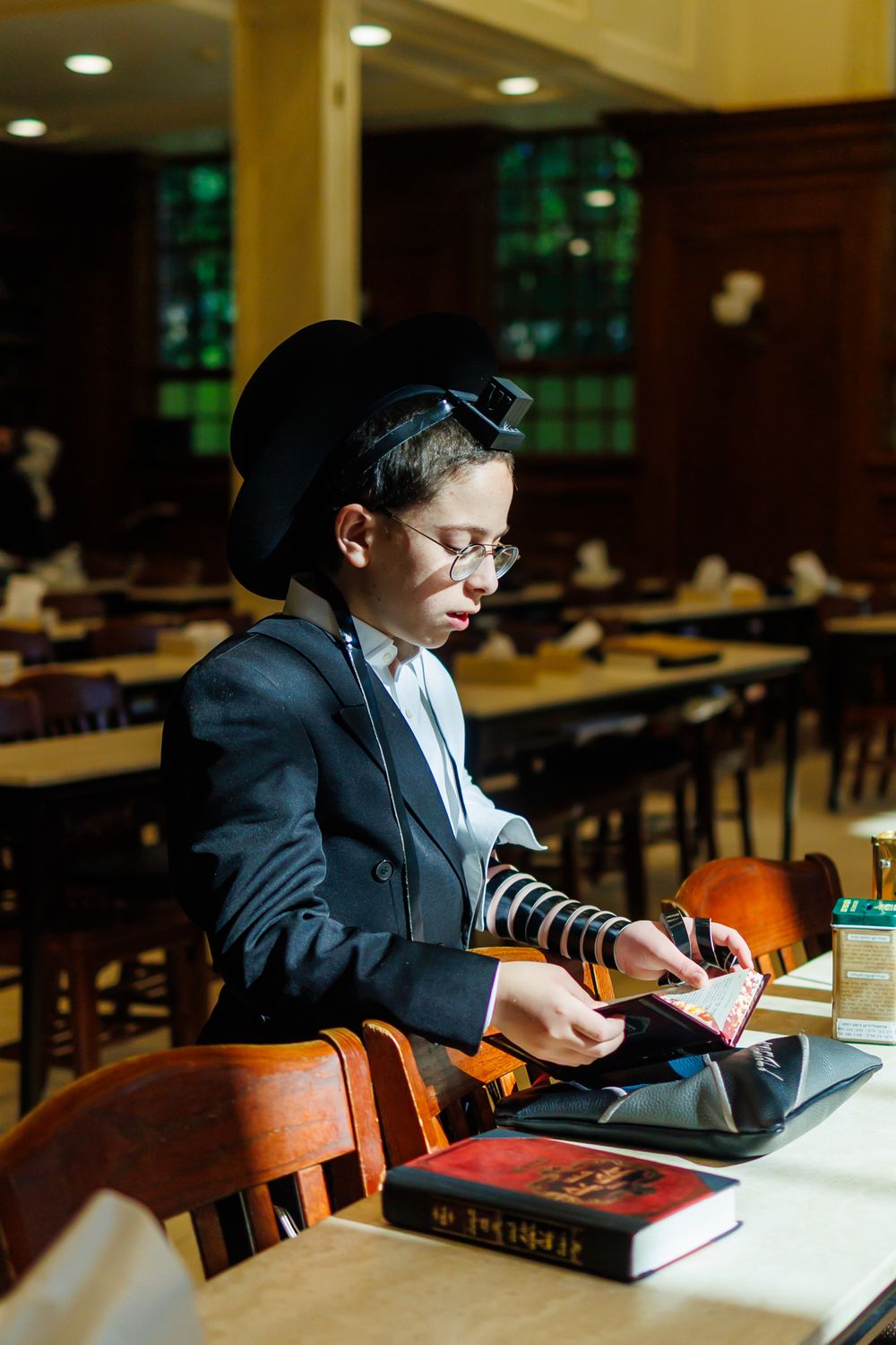 Student studies at a wooden library table wearing traditional religious garments and reading from sacred texts.