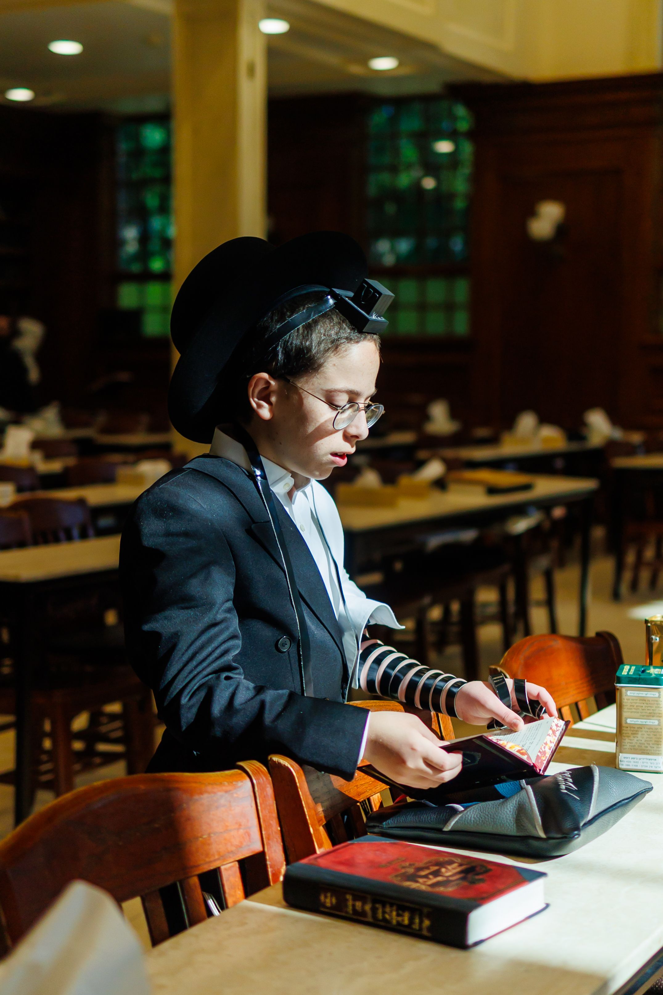Student studies at a wooden library table wearing traditional religious garments and reading from sacred texts.