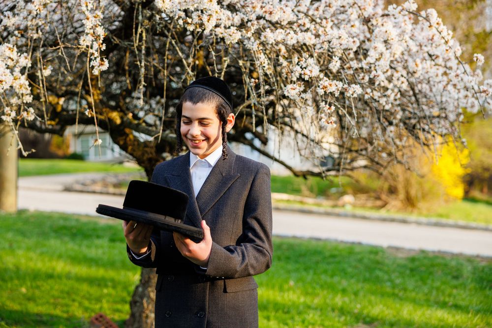 Young man in suit reading book under blooming cherry tree in spring park.
