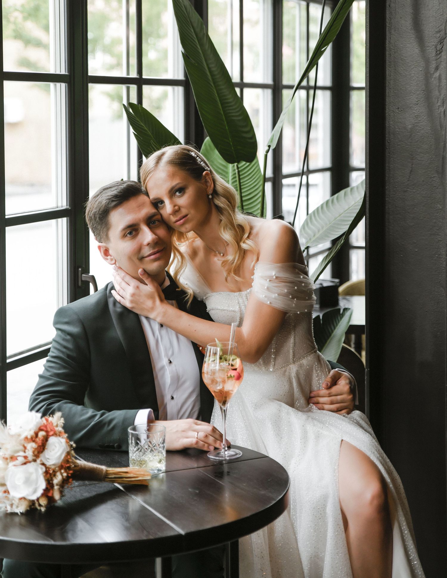 Wedding couple enjoying champagne in an intimate indoor setting with tropical plants.