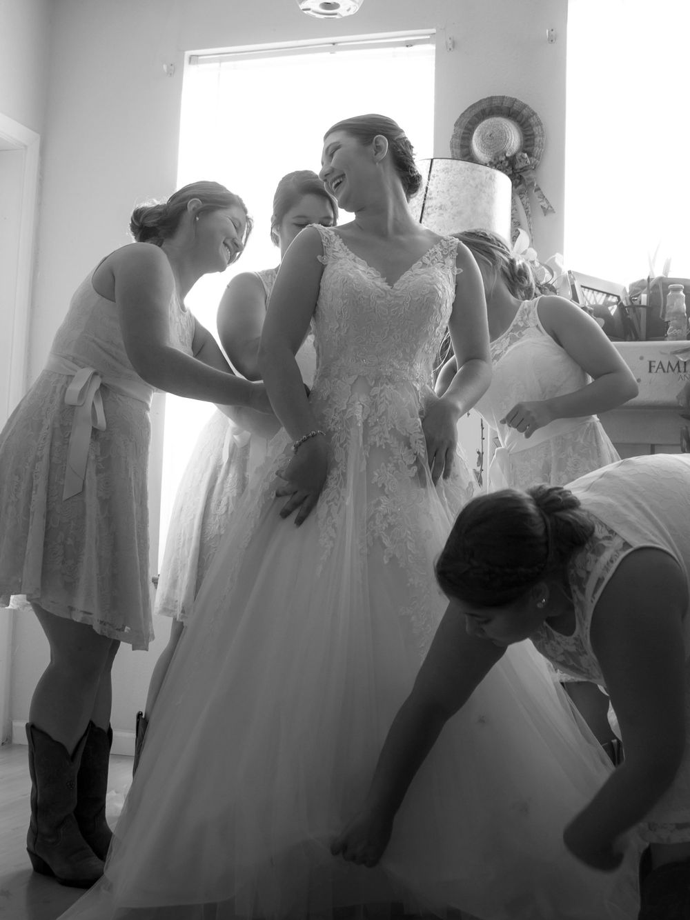 A bride and her bridesmaids assist her in putting on her wedding dress, capturing a moment of joy and support.