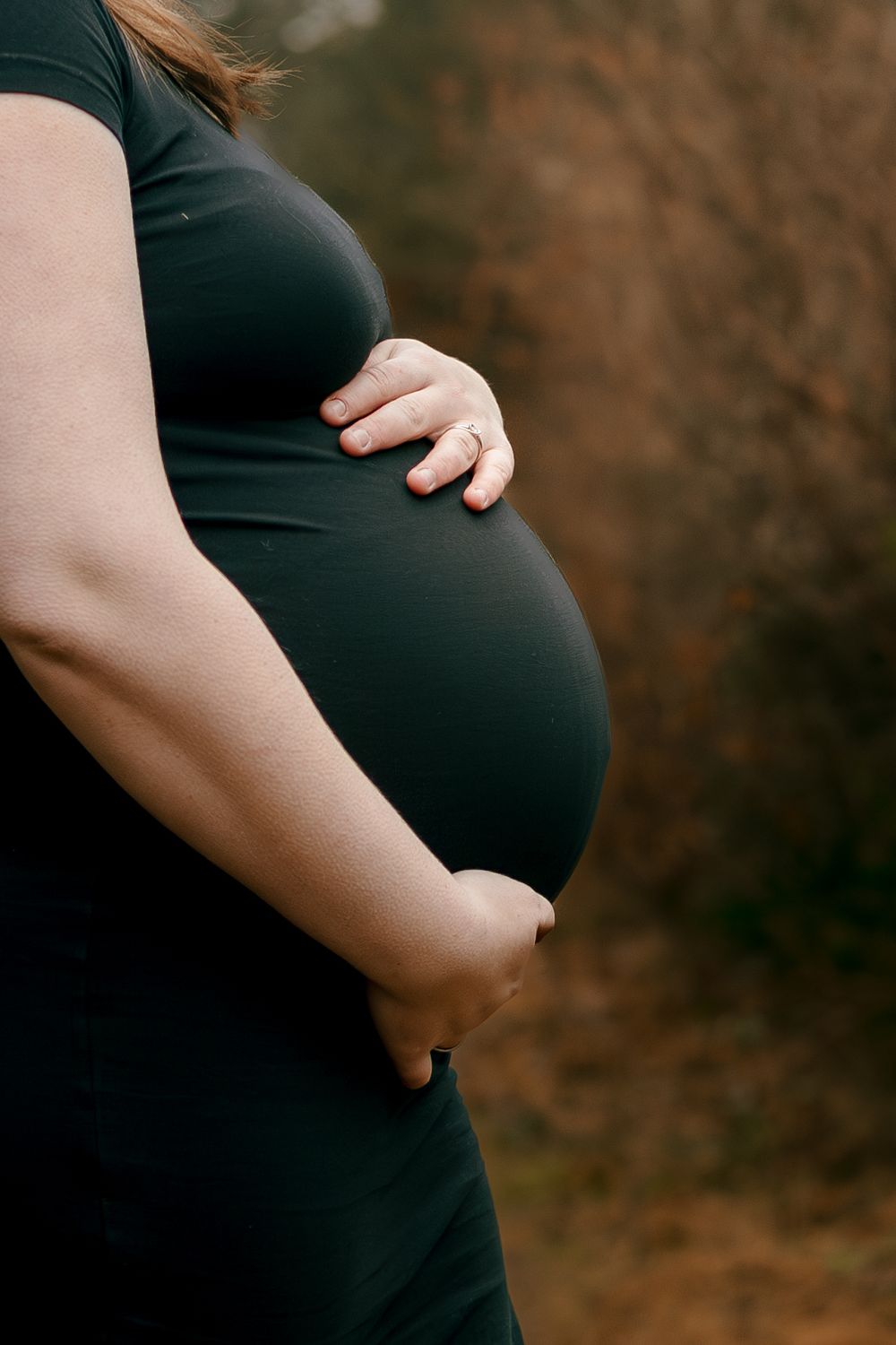 Close-up view of pregnant belly in black dress with hands gently resting on the curves of the baby bump.