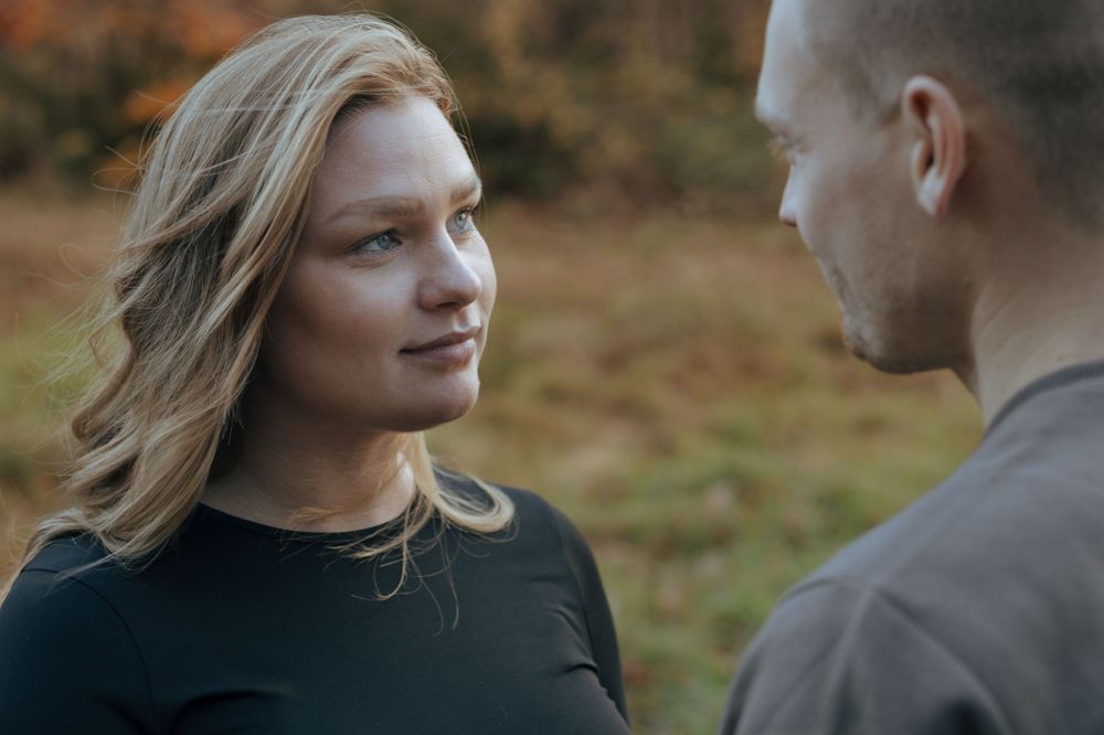 A gentle outdoor interaction between two people wearing dark sweaters against an autumn background.