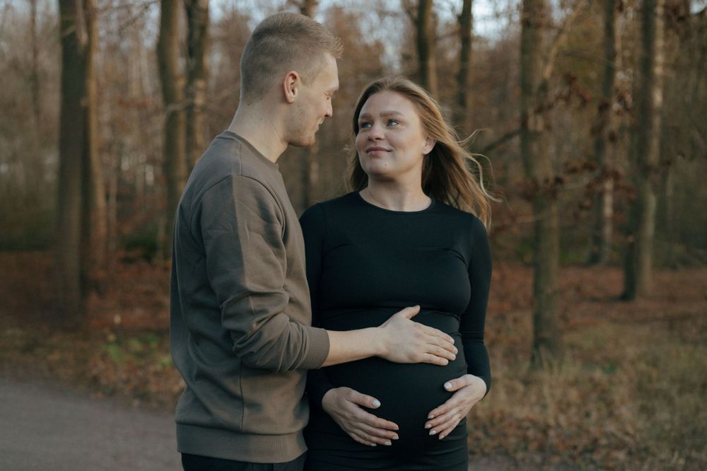 A couple shares an intimate moment on a walking path in an autumn forest while expecting a baby.