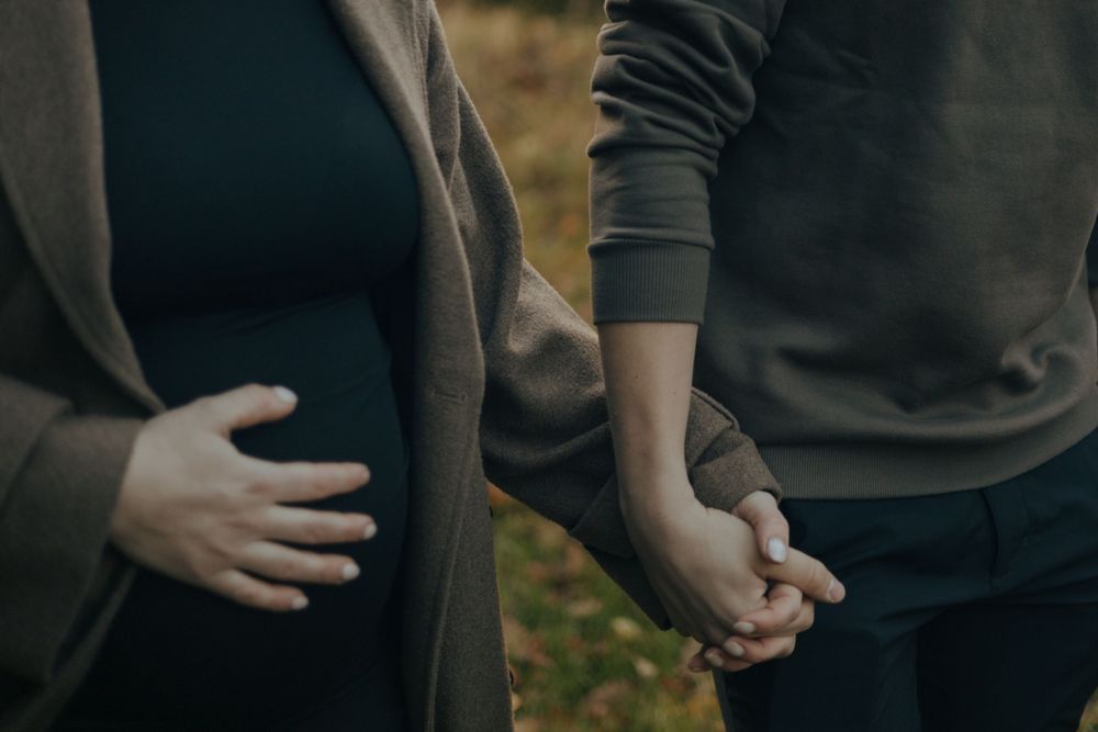 Close up photo of two people holding hands wearing dark clothing outdoors with blurred foliage in the background.