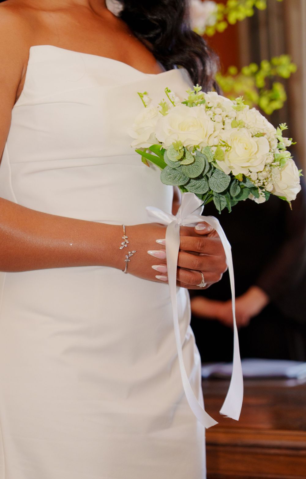 Wedding bouquets of white flowers and greenery are held by bridesmaids wearing white dresses in a church setting.
